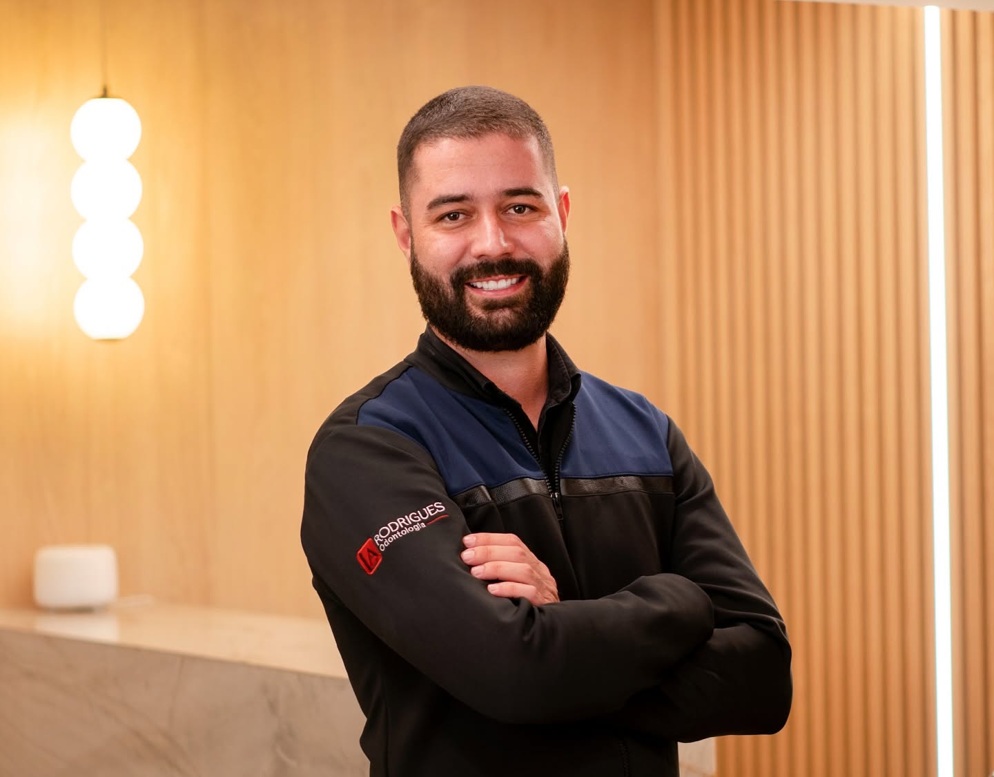 Dr. Luiz Antonio Rodrigues, fundador da LA Rodrigues Odontologia, sorrindo de braços cruzados na recepção da clínica